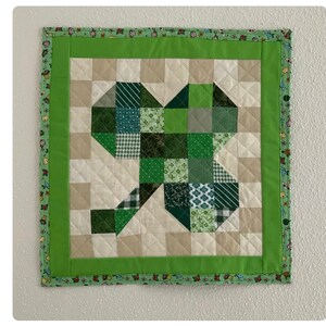May include: A green and white patchwork quilt with a shamrock design. The quilt is framed with a green border and a white and green border. The quilt is hanging on a white wall. Pinson Deborah &bull; Feb 13
