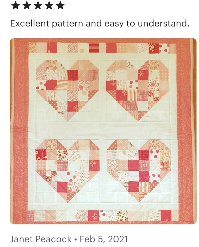 May include: A quilt with a white background and four pink hearts made of patchwork fabric. The hearts are made of various shades of pink, red, and white fabrics with different patterns, including polka dots, stripes, and floral prints. The quilt is bordered with a solid pink fabric.