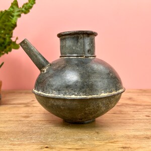 May include: A vintage, grey metal watering can with a round body and a spout. The can has a worn, rustic look.