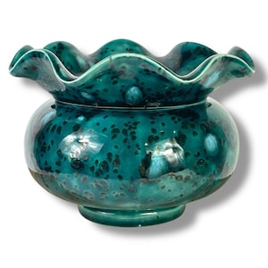 Peut inclure: Un bol en céramique turquoise avec un bord festonné. Le bol a un corps rond et une base en piédestal. La surface est mouchetée de taches brun foncé, et le glaçage a une finition brillante. Le bol est probablement à des fins décoratives.