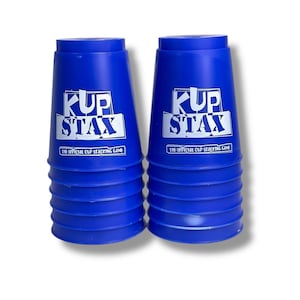 May include: Two vertical stacks of blue plastic cups for the Kup Stax cup stacking game. Each cup features the white printed text Kup Stax and the official cup stacking game logo on the front. The cups are smooth, cylindrical, and uniform.