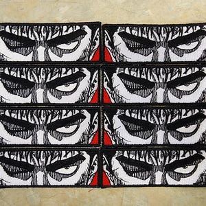 May include: Eight rectangular patches featuring a detailed illustration of a character's intense eyes and brow. The design is primarily black and white, with red accents on the edges. The patches are arranged in a grid.