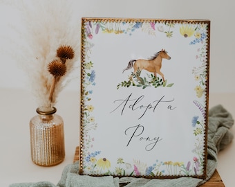 May include: A gold-framed sign with a floral border and a watercolor illustration of a brown horse. The sign says "Adopt a Pony" in a cursive font.