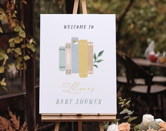 May include: A white sign with the text "Welcome to Lilliana's Baby Shower" and a stack of colourful books with a small flower on top. The sign is on a wooden easel in front of a bouquet of white and peach flowers.