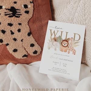 Op de afbeelding: Een witte uitnodigingskaart met gouden letters die "two WILD" zegt en een aquarel-illustratie van een leeuw, een giraf en een olifant toont. De tekst op de kaart luidt: "Nodig je uit om Davids 2e verjaardag te vieren, 12 augustus, 14:00 uur, The Birthday Play House, 1001 Garden Lean, Portland, RSVP: Linda voor 10 mei op 123.321.1234".