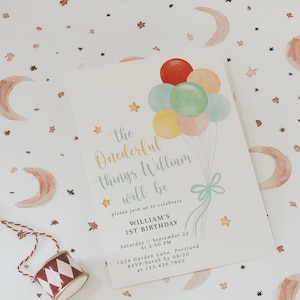 Puede incluir: Una ilustración de acuarela de una invitación de cumpleaños con un tema caprichoso. La invitación presenta un grupo de globos coloridos, estrellas y medias lunas. El texto dice "the Onederful things William will be" e incluye detalles para la fiesta del primer cumpleaños de William.