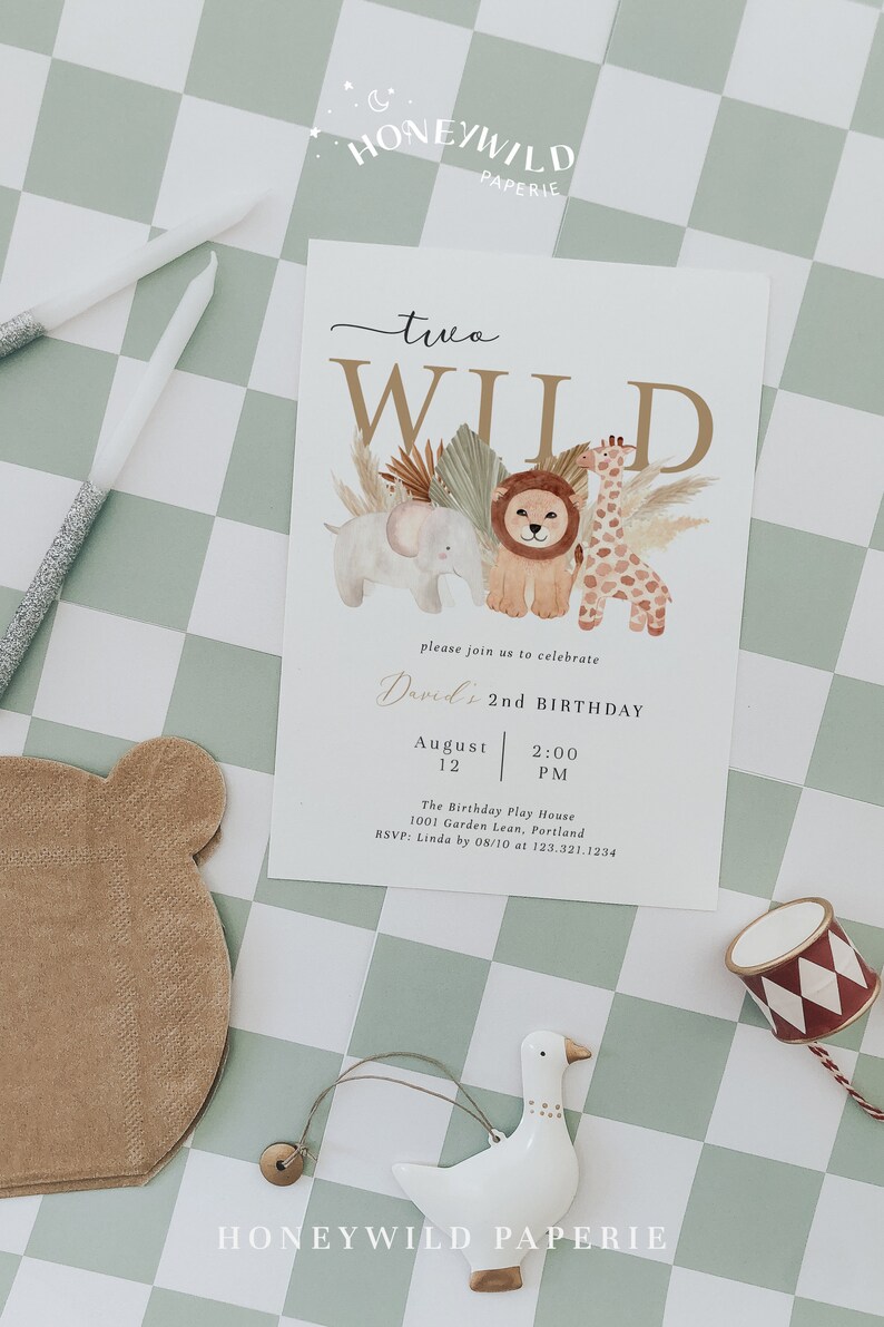 Op de afbeelding: Een witte kaart met een gouden en bruine illustratie van een leeuw, een giraffe en een olifant. De tekst "two WILD" staat in gouden letters. De kaart is een verjaardagsuitnodiging voor David's 2e verjaardag. De uitnodiging bevat de datum, tijd en locatie van het feest.
