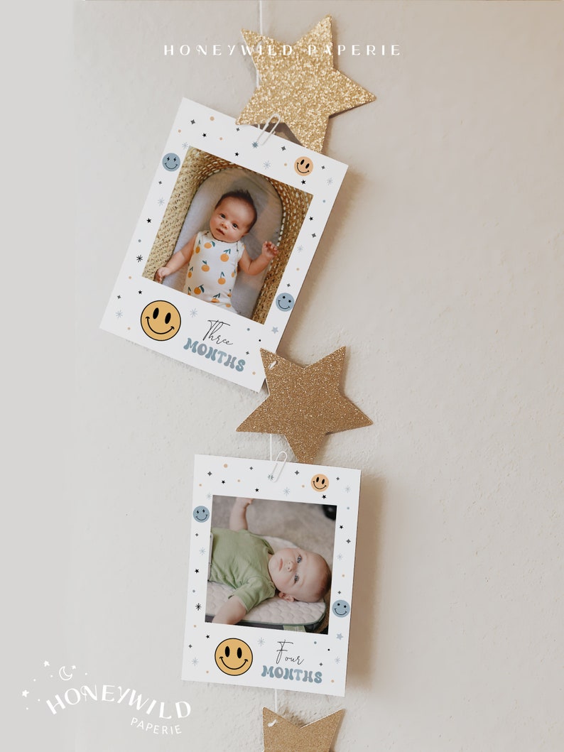 May include: A set of two white photo cards with a smiling face and the text "Three Months" and "Four Months" on each card. The cards are decorated with blue and yellow smiley faces and stars. The cards are hanging from a string with gold glitter stars.