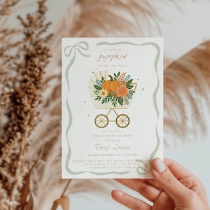 Puede incluir: Invitación a un baby shower con fondo crema y borde verde claro. La invitación presenta un cochecito con una calabaza y arreglos florales. El texto dice "A Little Pumpkin is on the Way!" y los detalles del baby shower de Emily Dawson.