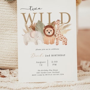 Op de afbeelding: Een witte uitnodigingskaart met gouden letters die een tweede verjaardagsfeestje voor een kind aankondigt. De uitnodiging bevat een aquarel-illustratie van een leeuw, een giraffe en een olifant met tropische planten. De tekst luidt "two WILD David's 2nd BIRTHDAY August 12 2:00 PM The Birthday Play House 1001 Garden Lean, Portland RSVP: Linda by 08/10 at 123.321.1234 HONEYWILD PAPERIE".