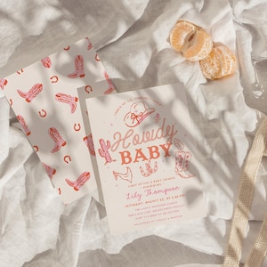May include: A baby shower invitation with a western theme. The invitation features the words "Howdy Baby" in a pink script font, along with illustrations of a cowboy hat, boots, and a cactus. A matching card with pink cowboy boots and horseshoes is also present.