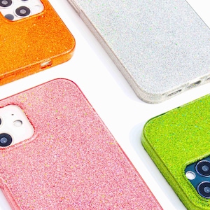 May include: Four glittery phone cases in orange, silver, pink, and green. Each case has a camera cutout and a smooth, rounded edge. The cases are designed to fit a smartphone.