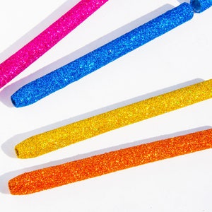 May include: Four glitter-covered pens in pink, blue, gold, and orange. The pens are arranged in a fan shape on a white background.