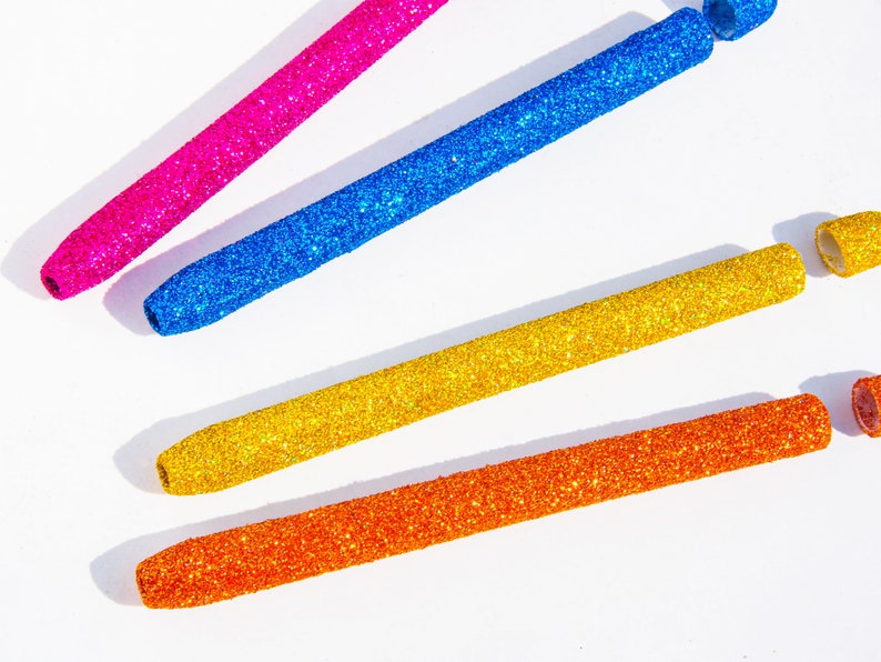 May include: Four glitter-covered pens in pink, blue, gold, and orange. The pens are arranged in a fan shape on a white background.