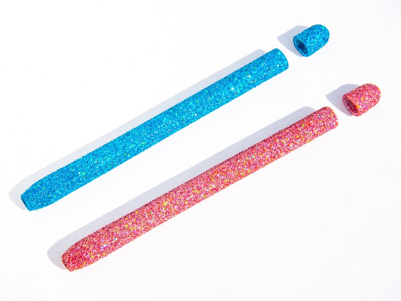 May include: Two glitter-covered makeup applicators, one blue and one pink, with the caps removed.