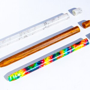 May include: Three different types of pens with colorful designs and caps. The pens are made of wood, marble, and tie-dye.
