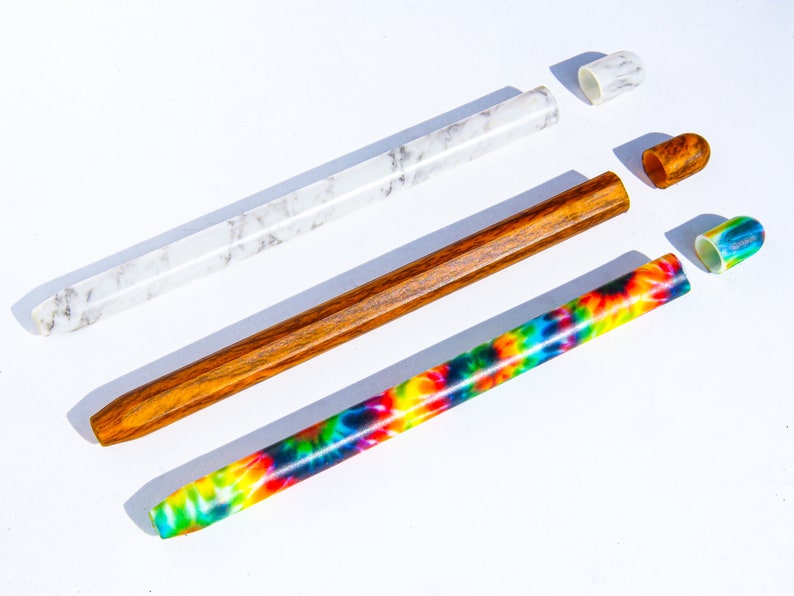May include: Three different types of pens with colorful designs and caps. The pens are made of wood, marble, and tie-dye.