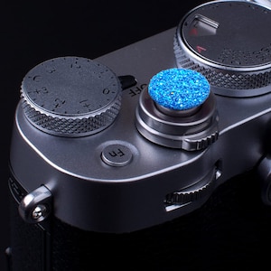 May include: A silver camera with a blue jeweled button and a dial with numbers 0-5 and letters C, +3, +2, +1, and -1.