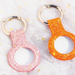 May include: Two keychains with silver rings and sparkly, colorful, round charms. The keychain on the left is pink and the keychain on the right is orange.