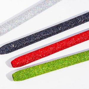 May include: Four glitter-covered pens in different colors: silver, black, red, and green. The pens are arranged in a diagonal line on a white surface.