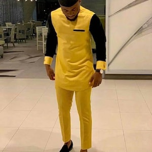May include: A man wearing a yellow and black outfit with black shoes. The outfit includes a long-sleeved shirt with a black collar and cuffs, and matching pants. The man is wearing a black hat.
