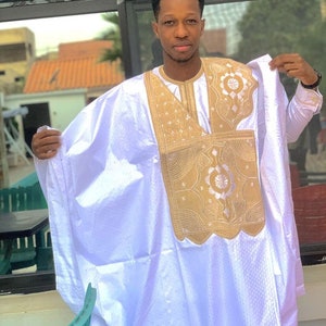 May include: A white long-sleeved robe with gold embroidery. The robe has a high collar and a long, flowing design. The embroidery is intricate and features geometric patterns.