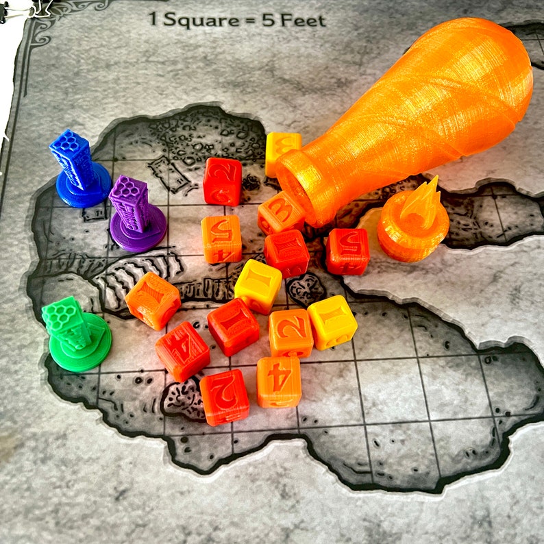 May include: A set of colorful dice with numbers 1 through 6, a small orange ceramic bottle, and a small orange ceramic flame. The dice are arranged on a gray and white gridded surface with the text "1 Square = 5 Feet".