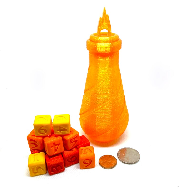 May include: A set of orange and yellow dice with numbers 1 through 6, stacked in a pyramid shape. A tall, orange, 3D printed bottle with a flame-shaped top sits next to the dice.