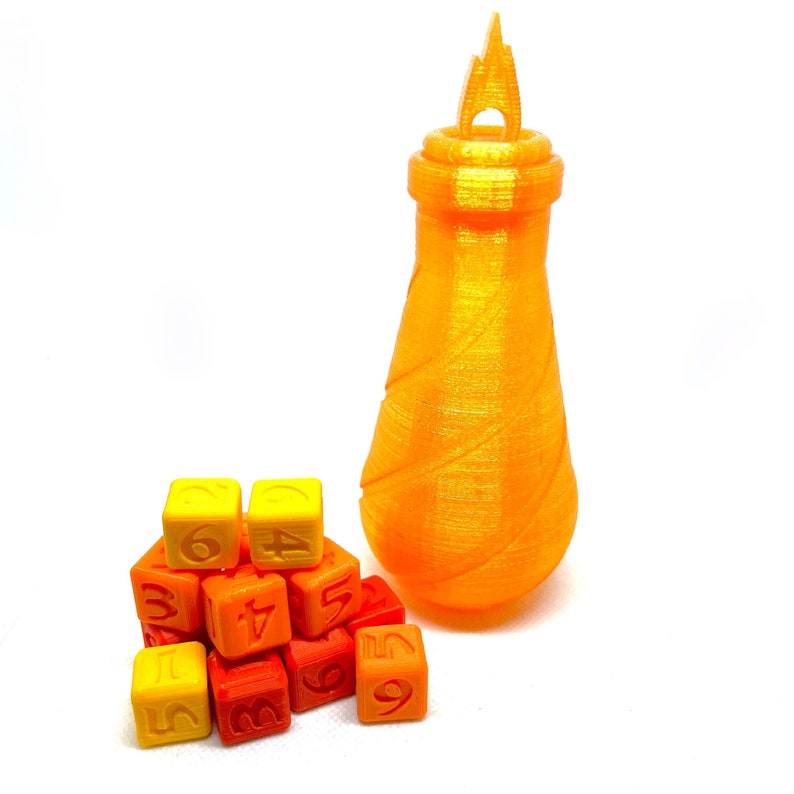 May include: A set of orange, yellow, and red dice with numbers 1 through 6. The dice are stacked in a pyramid shape. A tall, orange, textured bottle with a flame-shaped top is in the background.