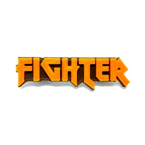 Puede incluir: La palabra "FIGHTER" impresa en 3D en naranja con un contorno marrón.