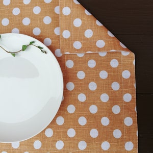 May include: A white ceramic plate sits on a brown and white polka dot placemat. The placemat has a linen texture and white polka dots on a brown background.