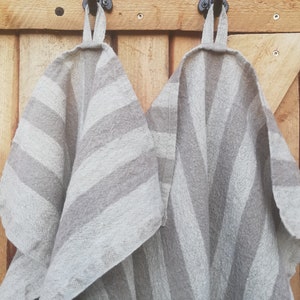 May include: Two gray and white striped kitchen towels hanging on black hooks attached to a wooden wall.