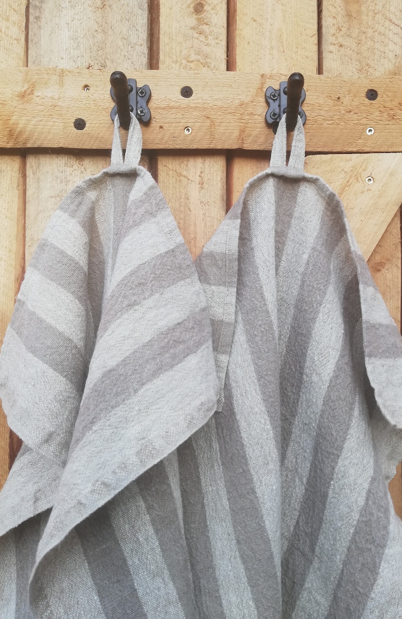 May include: Two gray and white striped kitchen towels hanging on black hooks attached to a wooden wall.