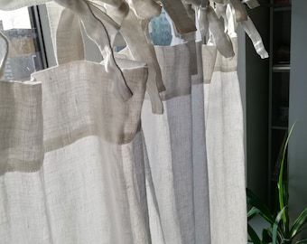 May include: Off-white linen curtains hanging in front of a window. The curtains are tied with matching fabric ties. The sunlight filters through the fabric, creating soft shadows. The curtains are a neutral color, suitable for various interior design styles.