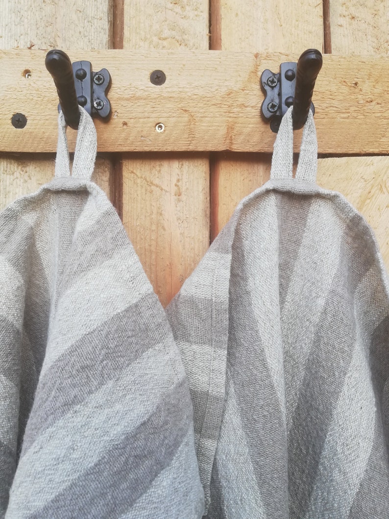 May include: Two gray and white striped linen tea towels hanging on black hooks attached to a wooden wall.