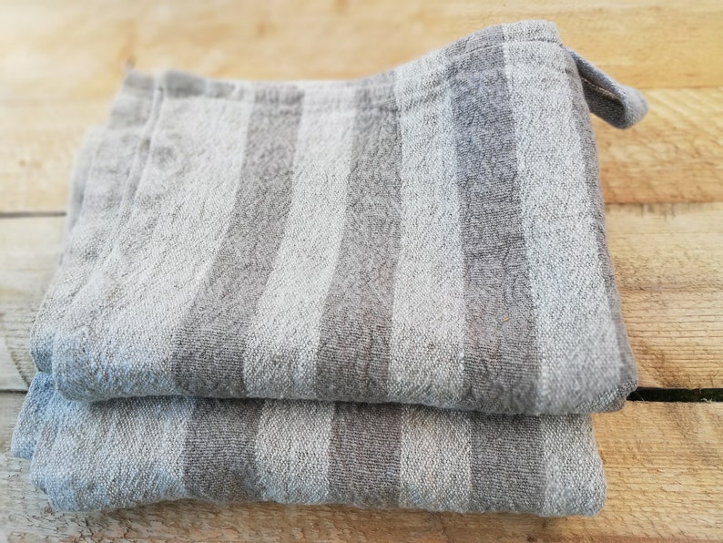 May include: Two gray and white striped linen kitchen towels folded on top of each other. The towels have a textured woven pattern.