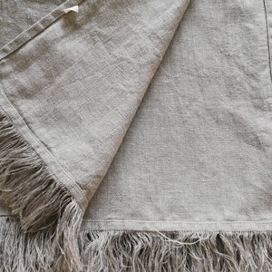 May include: A light gray linen throw blanket with a fringe border. The blanket is folded in half and the fringe is visible on both sides.