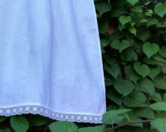 May include: White sheer curtain with a white lace trim hanging in front of a wooden wall covered in green vines.