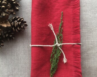 May include: Red linen napkin with frayed edges, tied with twine and a sprig of greenery.