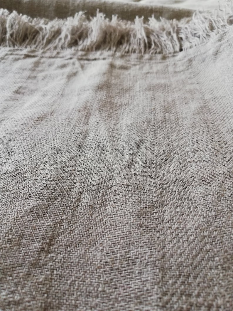 May include: Close-up of a light brown linen fabric with a frayed edge. The fabric has a woven texture and a subtle sheen.