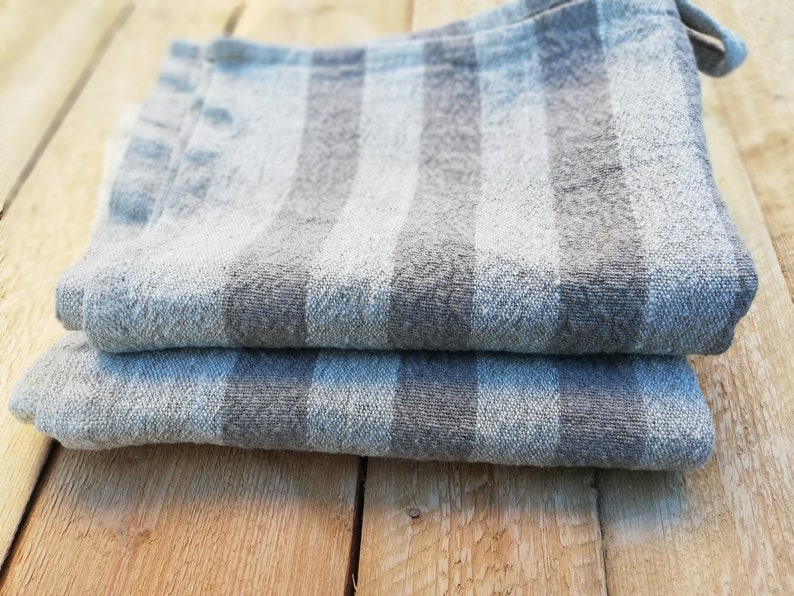 May include: Two gray and white striped kitchen towels folded on a wooden surface.