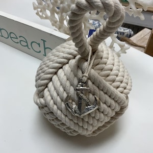 May include: A white rope doorstop shaped like a knot with a silver anchor charm.