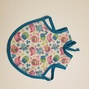 May include: A turquoise blue baby bib with a white background and a pattern of colorful owls and flowers.
