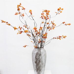 May include: A vase with a textured, gray and brown finish holds a bouquet of dried branches with orange leaves.