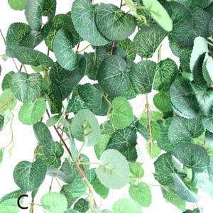 May include: A close-up of a green artificial vine with round leaves. The vine is hanging down and the leaves are arranged in a random pattern.
