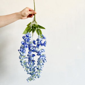 Pu&ograve; includere: Un mazzo di fiori di glicine artificiali con fiori blu e foglie verdi.