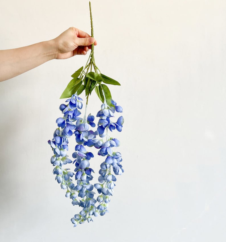 Pu&ograve; includere: Un mazzo di fiori di glicine artificiali con fiori blu e foglie verdi.