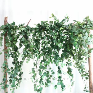 May include: Artificial green ivy garland hanging from a wooden frame. The garland is made of plastic leaves and vines and is perfect for adding greenery to any space.