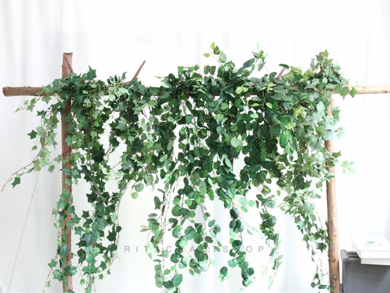 May include: Artificial green ivy garland hanging from a wooden frame. The garland is made of plastic leaves and vines and is perfect for adding greenery to any space.