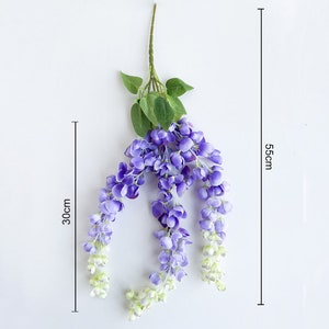 Pu&ograve; includere: Un lungo filo di fiori di glicine artificiali con fiori viola e foglie verdi. I fiori sono disposti a cascata e il filo &egrave; lungo circa 56 cm e largo 30 cm.